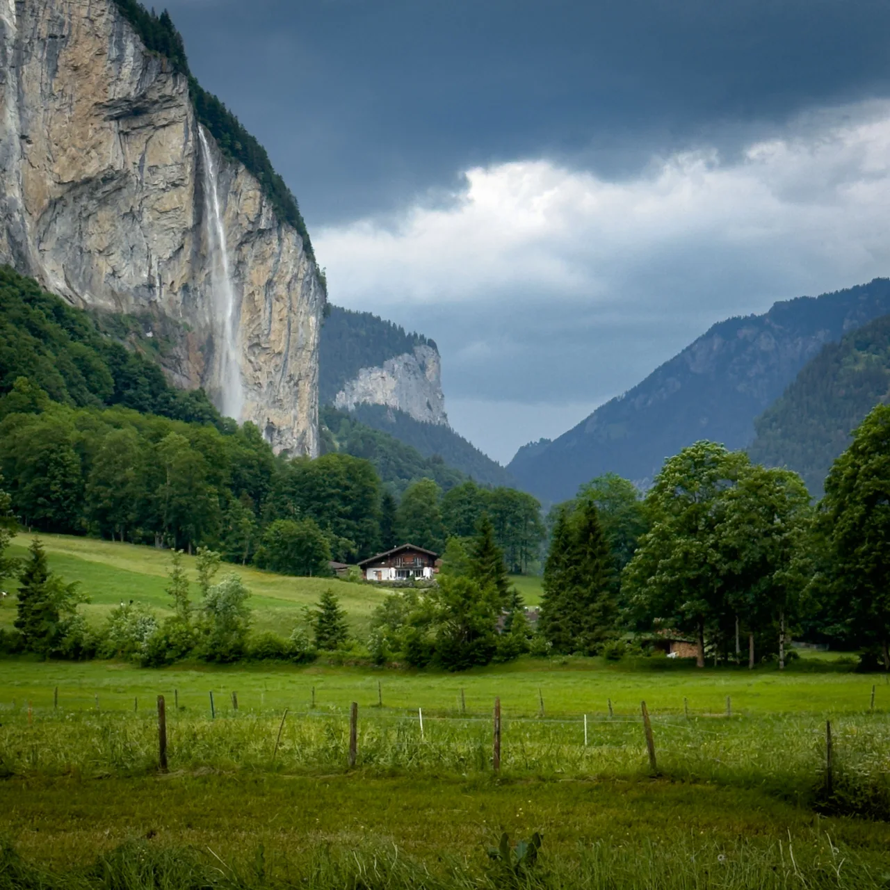 Traditional house and large waterfall amongst the green landscape of the Lauterbrunnen Valley
